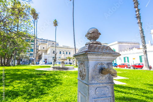 Old water tap on the virgilio park in brindisi, surrounded by buildings and cars. Park in the centre of brindisi old town
