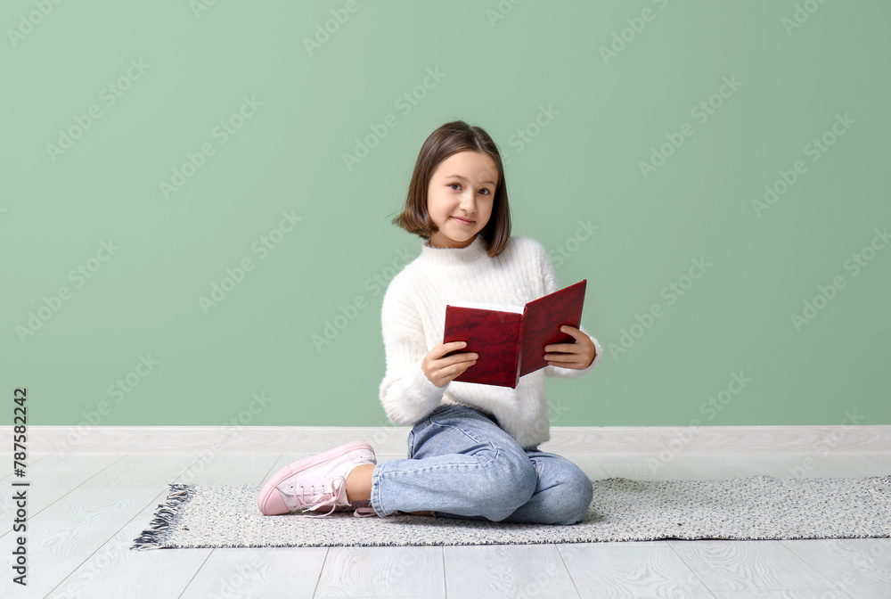 Little girl reading books while sitting on floor near green wall Little girl reading books while sitting on floor near green wall