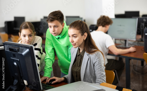 Female teacher and her students  young girl and boy  looking at monitor of PC during computer science lesson.