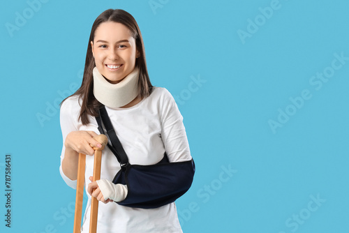 Injured young woman after accident with crutch on blue background