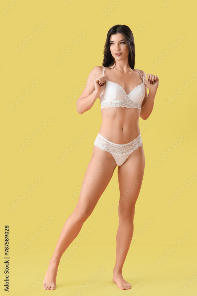 Naklejka premium Pretty young woman in white lace underwear on yellow background