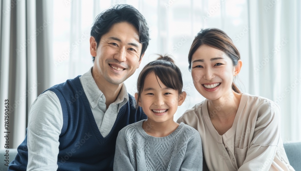 Obraz premium A young Japanese couple and their daughter, all smiling at the camera. Loving mother and father with kids enjoying time together at home sofa