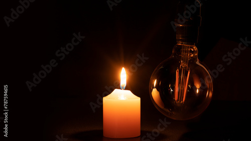 Blackout concept, turned off light bulb with no electricity hanging next to a burning candle