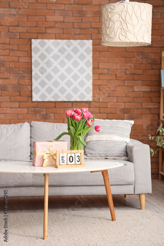 Vase with flowers, gift box and calendar on coffee table in living room photo