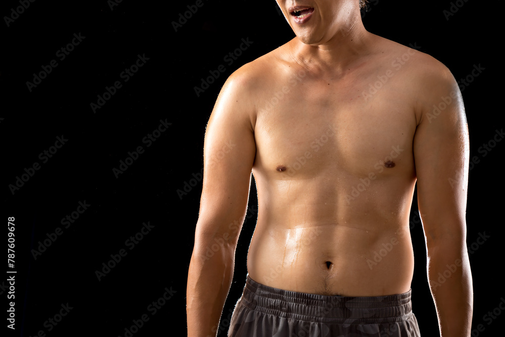 Fototapeta premium In a close-up shot against a black backdrop, the wet muscles of a young Asian man's body stand out, showcasing his physical prowess and determination