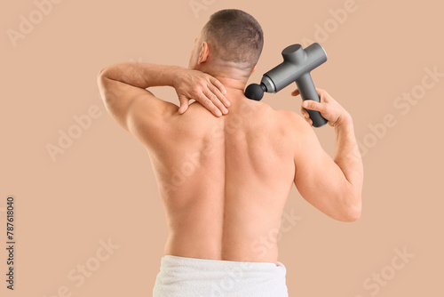 Muscular young man massaging his neck with percussive massager on beige background, back view