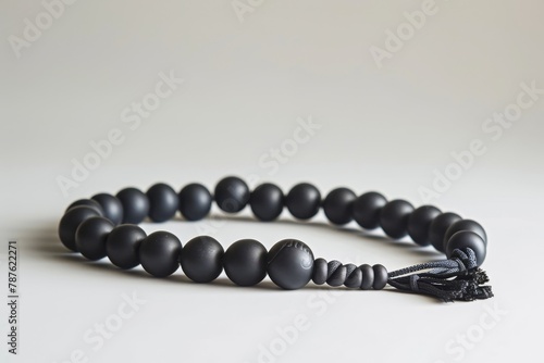 Black prayer beads with 33 stone knots on a matte surface against a white background photo