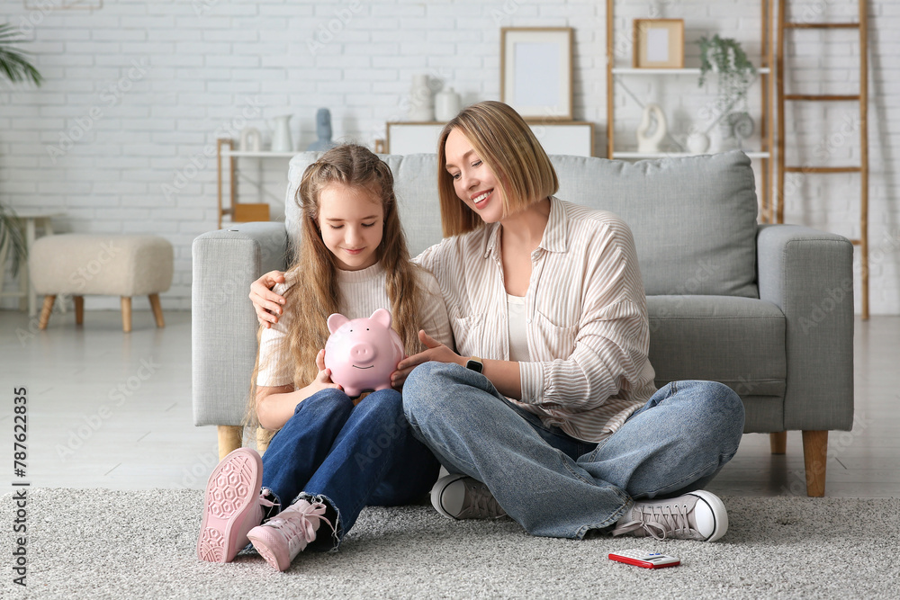 Mother and her daughter with piggy bank sitting on floor at home. Education savings concept