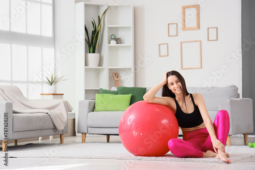 Sporty young woman sitting on floor with fitball at home