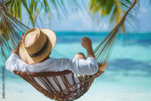 Man in a white shirt and straw hat relaxing in a hammock on a tropical beach. © evgenia_lo