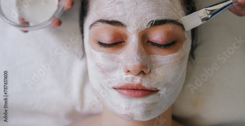 Young beautiful woman receiving white facial mask in spa beauty salon. Close-up view.