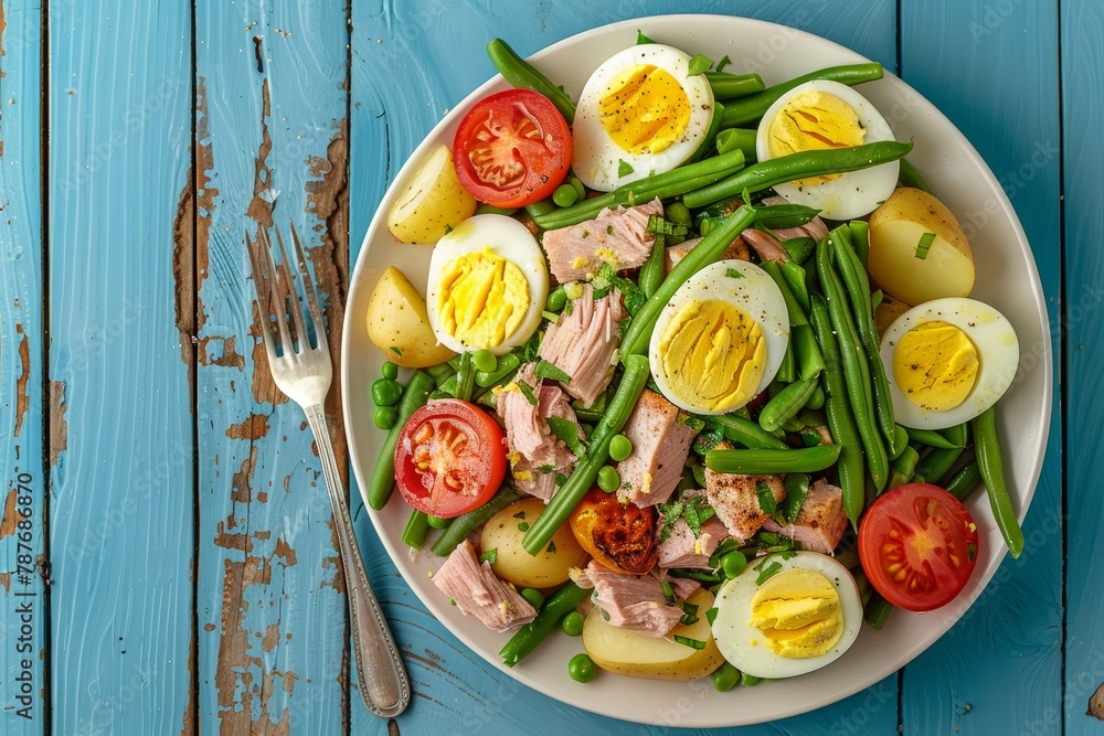 Traditional Nicoise Salad with tuna eggs potatoes green beans tomatoes over blue wooden background top view