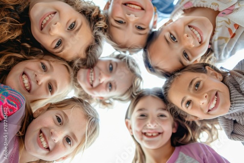 A group of happy, cheerful and cute children played together and had a great time. Group portrait of happy children huddled together, looking down at the camera and smiling. Low angle, view from below