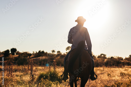 Man in hat riding a horse in the countryside at sunset photo