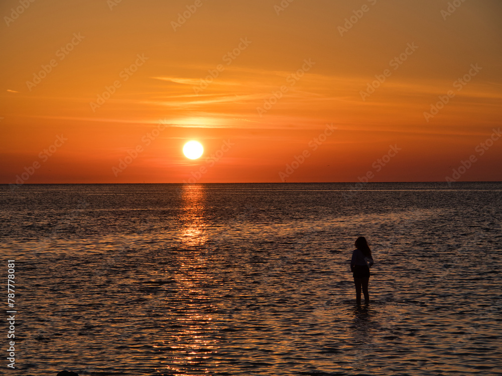 woman silhouette standing in water at beach during sunset woman silhouette standing in water at beach during sunset