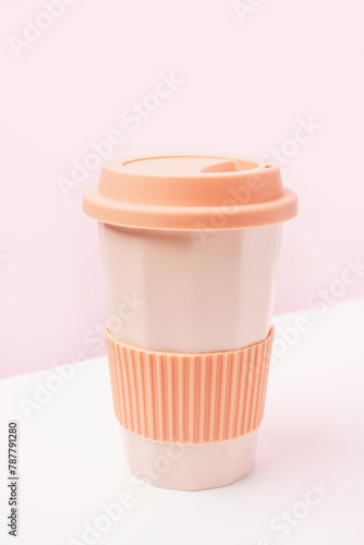 Reusable ceramic glass for coffee with silicone lid on pink and white background.
