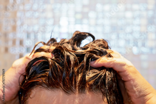 Woman washes her hair with shampoo on gray tiles background.