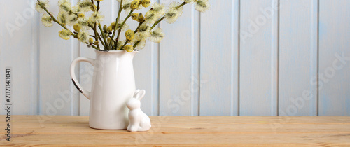 Easter banner with a rabbit figurine and a willow bouquet in a jug on the table. Easter background, spring holiday backdrop. empty space for your design.