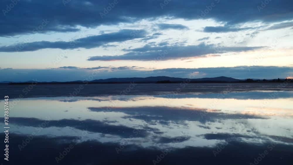 Beautiful landscape view of the lake with melting ice at sunset. A mirror image of the cloudy sky on the surface of the water. A calm scene. Beautiful landscape view of the lake with melting ice at sunset. A mirror image of the cloudy sky on the surface of the water. A calm scene.