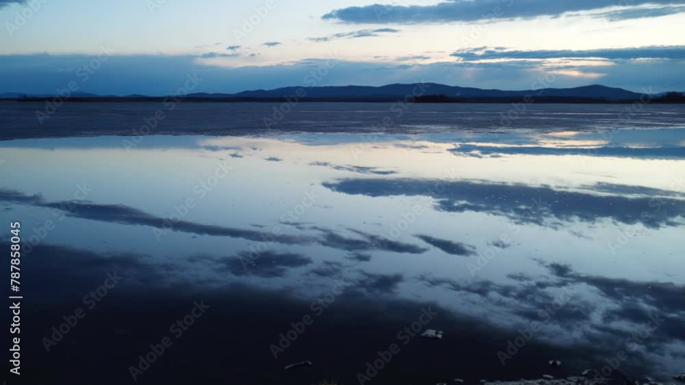 A landscape view of the lake with melting ice at sunset. A mirror image of the cloudy sky on the surface of the water. Love of nature. A landscape view of the lake with melting ice at sunset. A mirror image of the cloudy sky on the surface of the water. Love of nature.