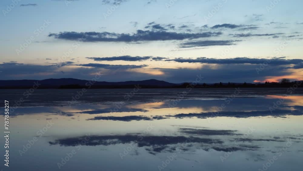 Beautiful landscape view of the lake with melting ice at sunset. A mirror image of the cloudy sky on the surface of the water. A calm scene. Beautiful landscape view of the lake with melting ice at sunset. A mirror image of the cloudy sky on the surface of the water. A calm scene.