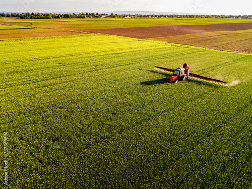 Drone shot of a tractor with sprayer in action on a vibrant green wheat farmland