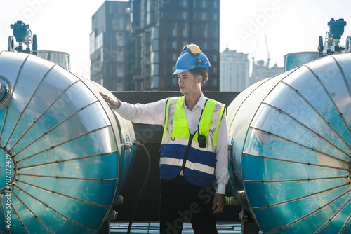 Building engineer reviews water tank systems atop a building with an urban backdrop of skyscrapers.