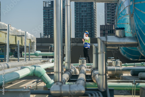 A professional engineer communicates via walkie-talkie on a building's rooftop, surrounded by piping and ductwork.
