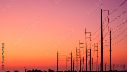 Silhouette two rows of electric poles with cable lines on curve country road against colorful orange sunset sky background after sundown