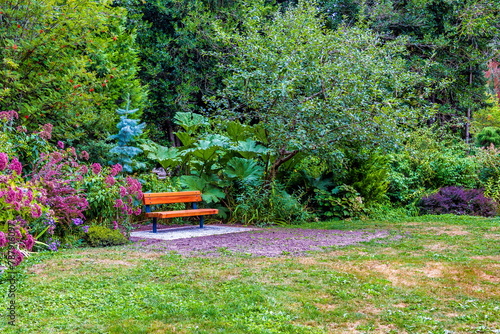 Spring. Resting place at Paulik Neighbourhood Park of Richmond City. Picnic Bench under the canopy of tree on a green lawn with flower beds among, British Columbia, Canada