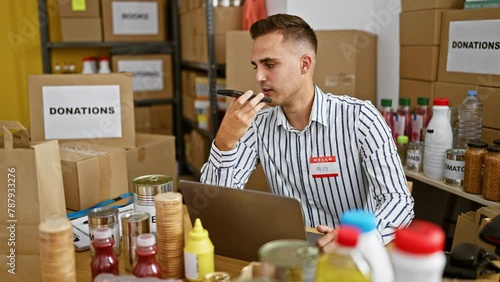 A young hispanic man named alex manages donations in a warehouse while using a phone and laptop.