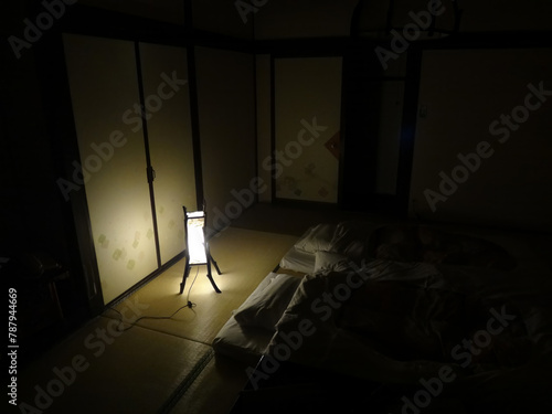 Japanese darkened bedroom interrior with tatami mat and two futon beds illuminated with small lamp