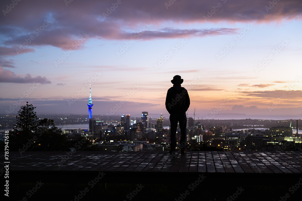 Man in silhouette looking at the views of Sky Tower and cityscape. Mt Eden summit at dawn. Auckland.