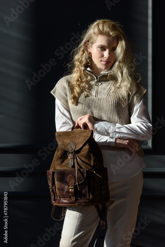 beautiful curly blond hair woman posing with a leather backpack
