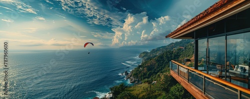 Modern cliffside villa overlooks the ocean with a paraglider soaring by, signifying luxury living and adventure. © Daniela
