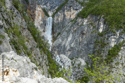 Boka waterfall in Slovenia, near Bovec. Easy trekking nature trail in the forest with the view of the immense waterfall overhanging the mountains visible from the road, long exposure photography. photo