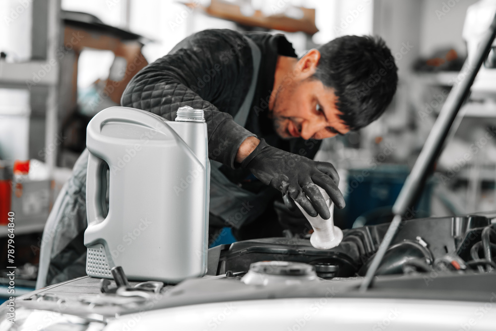 Obraz premium Close up of car service worker pouring new oil into car engine