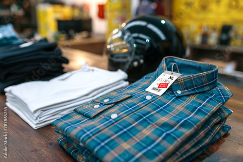 Detail of label with promotion price over a blue plaid shirt on shop with industrial style. Organized apparel stacks ready to sell on sales season on vintage clothes store. Black friday concept.