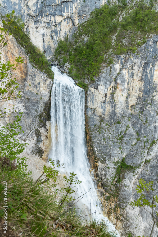 Boka waterfall in Slovenia, near Bovec. Easy trekking nature trail in the forest with the view of the immense waterfall overhanging the mountains visible from the road, long exposure photography. Boka waterfall in Slovenia, near Bovec. Easy trekking nature trail in the forest with the view of the immense waterfall overhanging the mountains visible from the road, long exposure photography.