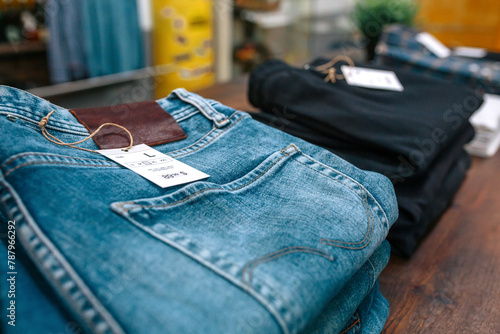 Detail of label with price and size over a blue jeans pants on industrial style store. Close up of organized apparel stacks over counter ready to sell on vintage clothes shop.
