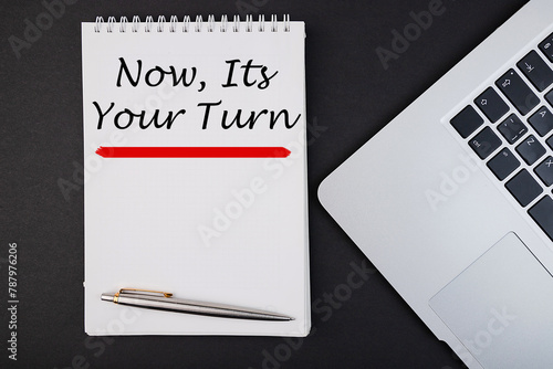 Now it's your turn text, inscription, phrase written in a notebook that lies on a dark table with a laptop and pen. Business concept.
