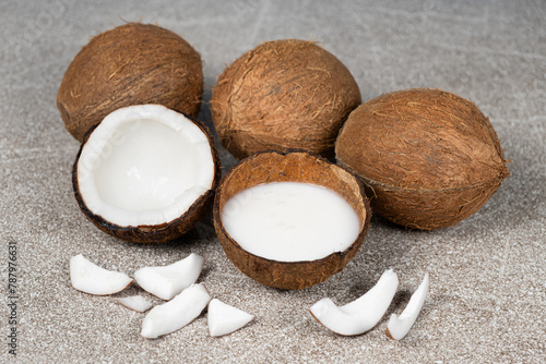 Coconut milk in coconut shell and half coconut, chopped flesh on grey background