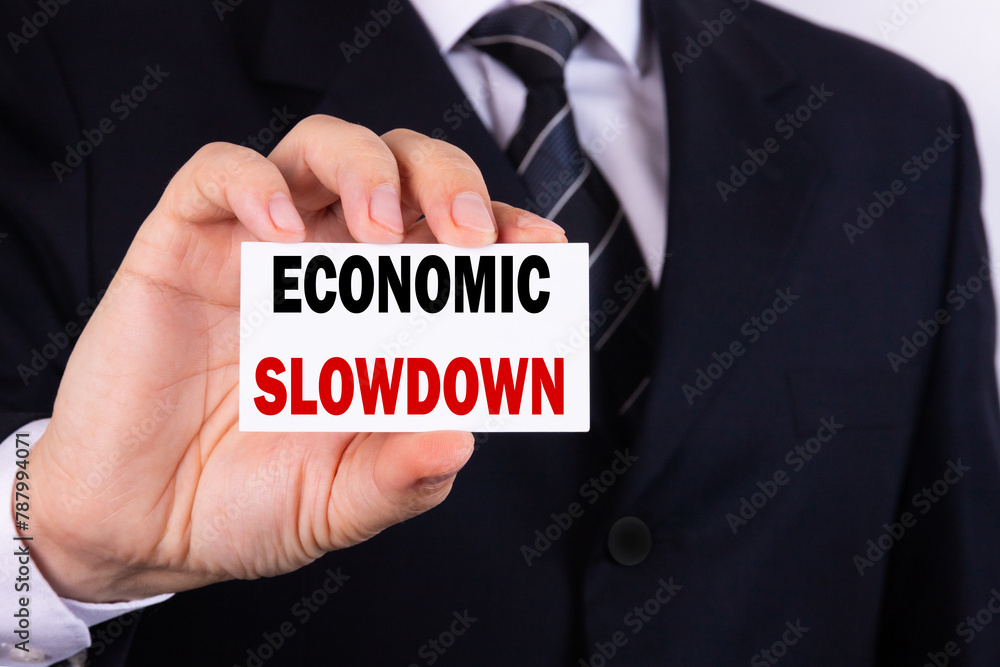 A businessman is holding a tablet with the text Economic Slowdown in front of him in his hands. Business concept. A businessman is holding a tablet with the text Economic Slowdown in front of him in his hands. Business concept.
