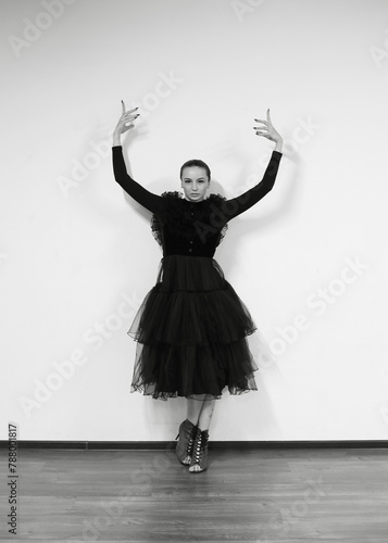 Ballerina on a white background, she is in a black dress. A brunette girl poses in front of the camera. Beautiful dancer, black and white style.