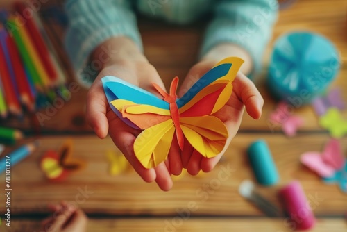 Child holding paper butterfly showing cut art crafts Funny colored paper butterfly on table in craft workshop