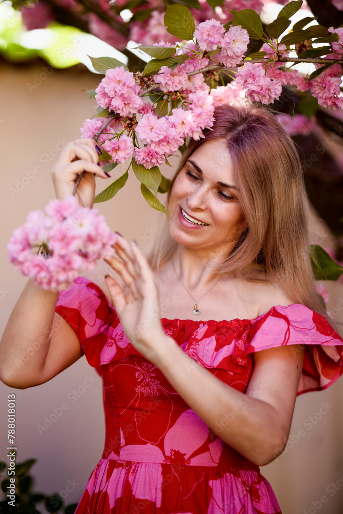 Obraz premium portrait of a blonde woman next to a blooming Japanese cherry tree on a spring day.