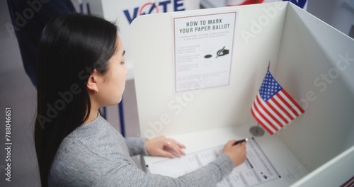 Obraz na plátně Asian woman comes to voting booth at polling station, makes choice and fills out paper bulletin
