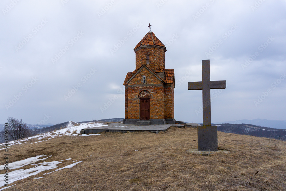 Didgori battle memorial, Georgia. Winter and snow, overcast. The small church is built of orange bricks with a cross on the dome. Nearby is a stone cross.