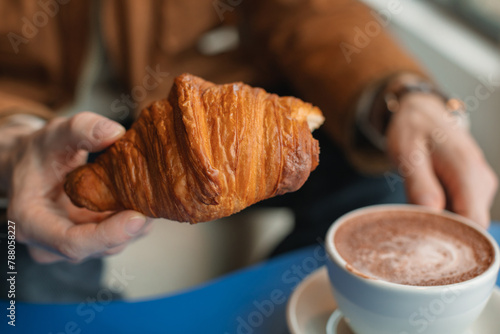 Close-up of a man sitting in a cafe eating a croissant and drinking a cup of coffee