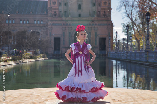 Girl dancing flamenco, posing looking at the camera, in typical flamenco dress, receiving the sun's rays, next to a lake in a beautiful square in Seville. Concept dance, flamenco, typical Spanish.